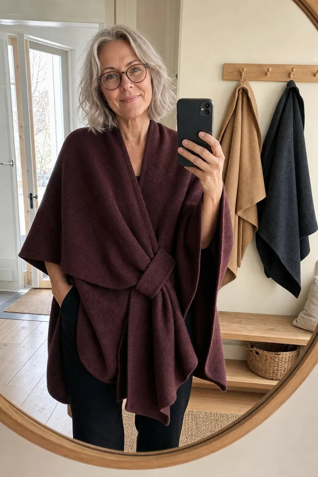 Kund i vinröd Lovelle Poncho framför hallspegeln, med en kamel och en mörkgrå på krokarna bredvid